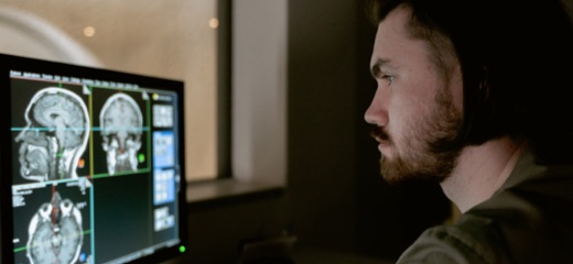 A dark-haired man with beard looking at a computer screen analysing a brain scan at hospital